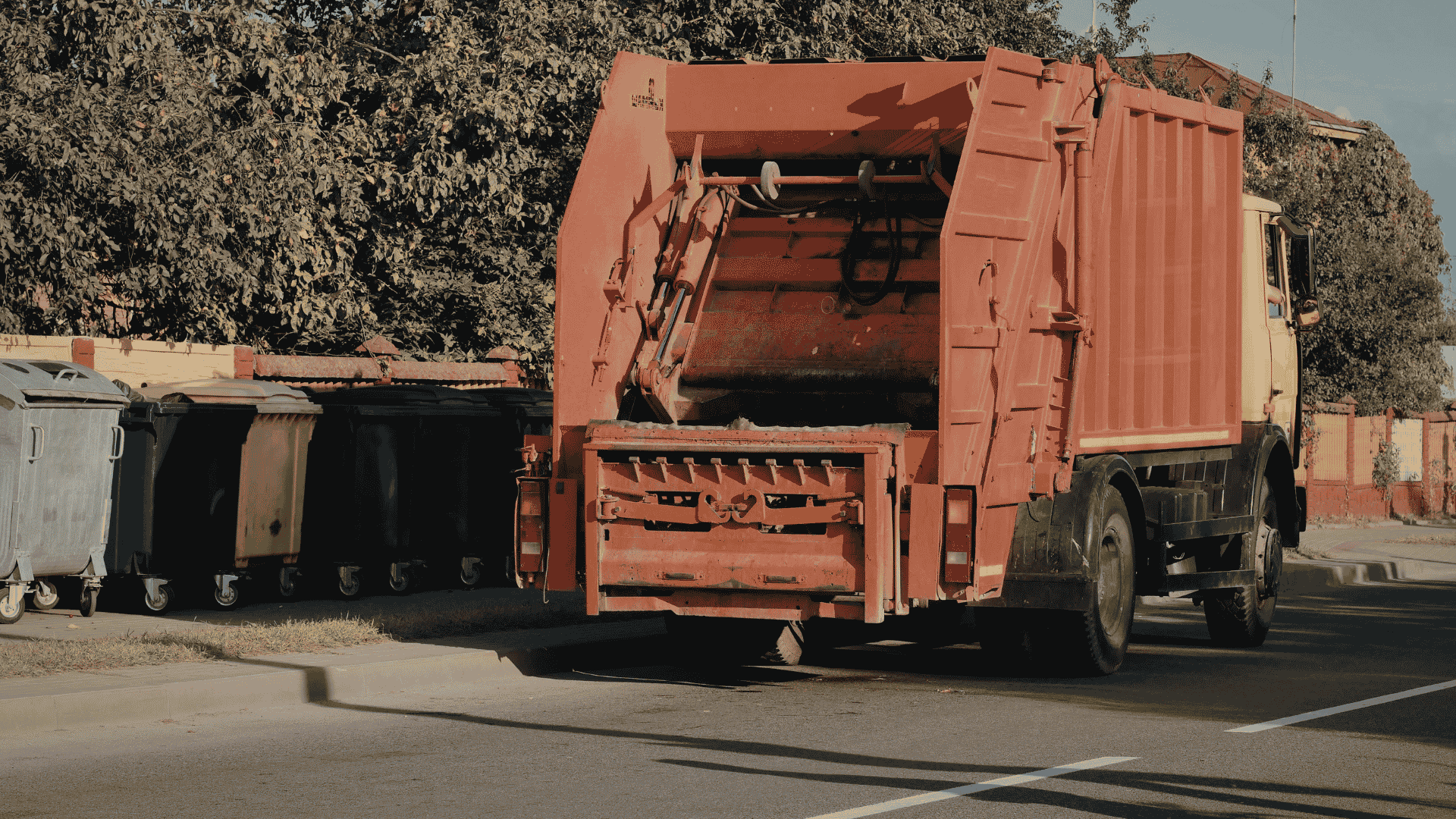 red garbage truck collecting dumpsters and waste containers