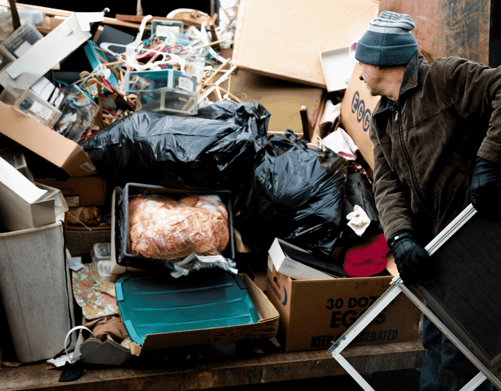 worker loading household junk and trash into dumpster container